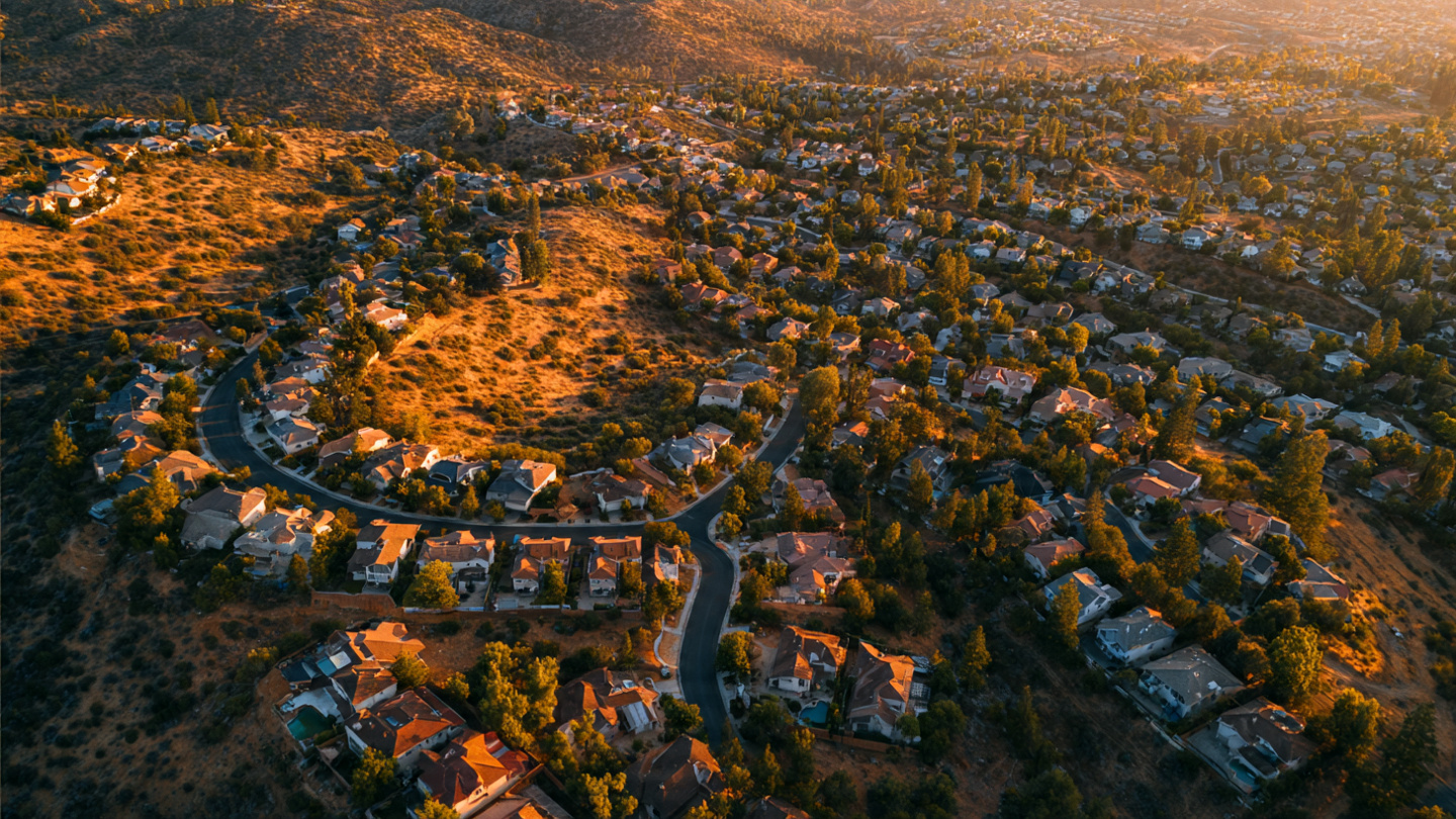 Aerial satellite view of a residential neighborhood at the wildland-urban interface with AI analysis overlay highlighting vegetation proximity and roof materials
